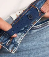 Pantalón de jean azul claro, modelo flare, con cintura elástica, trabillas para cinturón, bolsillos delanteros y traseros, y botón en forma de flor.