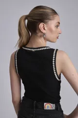 Remera negra ajustada al cuerpo, tipo musculosa, con escote redondo y ribetes en blanco con apliques de perlas en el contorno del cuello y las sisas.