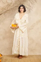 Vestido largo color crema con bordados florales en tonos pastel, escote en V con volados, mangas largas acampanadas y abertura frontal. Incluye lazo ajustable en la cintura.