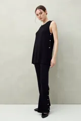 Pantalón negro de punto con calce relajado, caída fluida y botones dorados en los laterales.