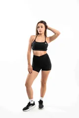 Conjunto deportivo blanco compuesto por un top con tirantes finos y logo en el pecho, y un short de tiro alto con diseño cruzado en la cintura.