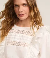 Blusa blanca de tricolina con volados en los laterales, cuello redondo, cierre por gota, mangas abullonadas largas y entremedios en el busto y en las mangas.