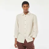 Camisa de lino color beige claro, de corte regular, con cuello clásico y mangas largas con puños abotonados.