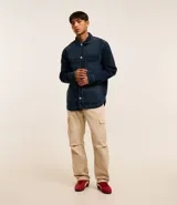 Camisa masculina oversized confeccionada en jeans azul oscuro, con cuello inglés, manga larga, puño ajustado, abotonado delantero y dos bolsillos cargo en el pecho.