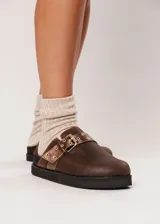 Zuecos marrones de cuero con hebilla metálica ajustable y plataforma baja.