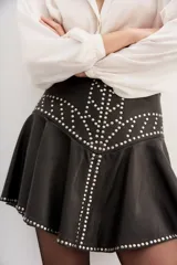 Minifalda negra de cuero ovino con forro de poliéster y tachas plateadas.