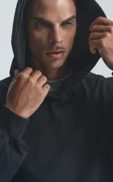 Hoodie negro de corte oversize con capucha, bolsillo tipo canguro y detalle de bolsillo con cierre en la manga izquierda.