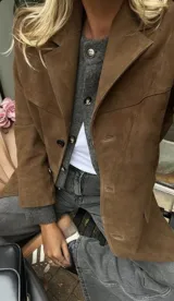 Blazer marrón de gamuza con cuello de solapa, cierre con botones y bolsillos frontales.