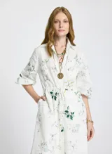 Vestido camisero midi blanco con estampado floral, cuello camisero, mangas 3/4 abullonadas, cierre frontal con botones y lazo ajustable en la cintura.