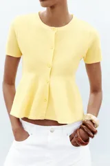 Chaqueta color amarillo claro de tejido de punto, con cuello redondo, manga corta, cierre frontal con botones y bajo evasé.