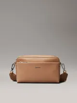 Bandolera Calvin Klein color marrón claro con estampado del logo de la marca. Tiene correa ancha ajustable, cierre de cremallera, bolsillo exterior delantero y bolsillo interior.