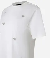 Blusa color crudo de algodón con cuello redondo y mangas cortas. Presenta bordados de lazos con perlas artificiales.