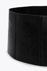 Cinturón fajín ancho de cuero negro con hebilla metálica cuadrada y detalle de flores labradas.