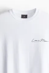 Remera blanca de algodón con cuello redondo y hombros caídos. Tiene un corte holgado y un pequeño estampado con la frase "Less is More" en el lado izquierdo del pecho.