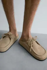 Zueco color beige de piel con acabado serraje, detalle de cordones y bordón en el empeine, plantilla acolchada, horma redonda y suela ultrafina a contraste.