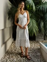 Vestido blanco de broderie con escote en V, corte bajo el busto y breteles finos cruzados en la espalda. Tiene forro interno a tono y largo midi.