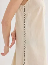 Vestido color crudo, de corte recto y largo a la rodilla, sin mangas y con escote en V. Presenta detalle de costura en zigzag a lo largo de los laterales.