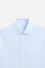 Camisa celeste a rayas verticales, de corte regular, confeccionada en algodón, con cuello italiano, manga larga con puños abotonados y cierre frontal con botones.