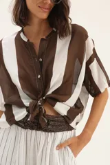Camisa marrón y blanca a rayas verticales, con cuello mao y mangas cortas. Se ata en la parte delantera.