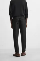 Pantalón negro de corte cropped, con cintura elástica ajustable con cordón, bolsillos laterales y traseros de vivo. El bajo tiene terminación con vuelta.