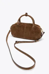 Bolso mini bowling color camel de serraje, con doble asa de mano y correa bandolera extraíble. Tiene un bolsillo interior con cremallera y cierre principal con cremallera y tirador.