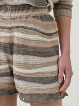 Short tejido de punto a rayas horizontales en tonos beige, blanco y marrón. Cuenta con cintura elástica y forro interno. El ruedo tiene un detalle calado.