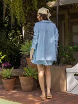 Camisa a rayas beige y blanco, de corte holgado, con cuello camisero y mangas largas fruncidas con lazos.