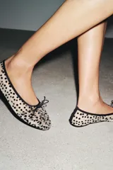Zapato tipo bailarina de malla color blanco con estampado de lunares negros, detalle de lazo en la puntera, tirador trasero y suela plana.