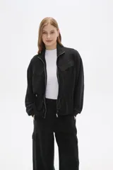 Campera negra de poliéster con cierre frontal, cuello alto, bolsillos con solapa en el pecho y cintura ajustable con cordón.