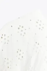 Camiseta blanca de cuello redondo y manga corta abullonada con elástico. Detalle de bordados perforados a tono.
