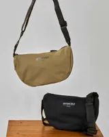 Bandolera de tela color beige con correa negra ajustable y cierre superior con cremallera. Estampado frontal con la palabra "INVENCIBLE" y el año "1964".