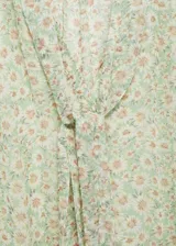 Blusa de gasa negra con estampado de margaritas blancas, cuello pico con lazo y cierre de botones frontal.
