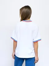 Remera blanca de corte clásico con cuello redondo y mangas cortas con puños tricolor (azul, blanco y rojo). Presenta el logo de Umbro bordado en el pecho izquierdo y el escudo del Club Nacional de Football bordado en el pecho derecho.