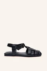 Sandalias franciscanas de cuero negro con tiras entretejidas y hebilla lateral.