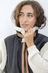 Chaleco negro de cuero con cuello y borde inferior de piel sintética negra. Cierre frontal con cremallera color cobre y detalles en cuero color tostado.