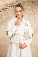 Campera color crema de algodón con estampado de flores, plumas y colibríes, con cuello camisero, cierre frontal con botones metálicos y mangas largas.