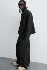 Pantalón negro de corte amplio, confeccionado en tejido de algodón con efecto lavado. Presenta bolsillos frontales, traseros de parche, tira multifunción y bolsillos laterales en las perneras. Cuenta con cierre frontal con cremallera y botón.