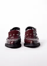 Mocasines color borgoña de cuero con punta fina, detalle de apliques metálicos y tira trasera con hebilla.