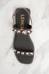 Sandalias bajas de cuero color marrón con apliques de tachas metálicas plateadas.