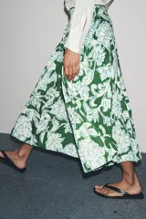 Falda midi de tiro medio con estampado floral en tonos blanco y celeste sobre fondo verde. Presenta detalle de tablas y cierre lateral con cremallera oculta.