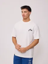 Remera blanca de hombre con logo de la marca Rusty estampado en el pecho y diseño a cuadros en la parte inferior trasera.