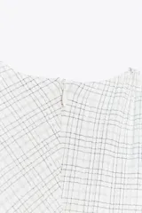 Vestido midi blanco con estampado de cuadros grises, cuello redondo y sin mangas. Presenta detalle drapeado en el frente y cierre oculto en la espalda.