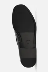 Zapato náutico de vestir color negro, con parte superior lisa, bordón, detalle de ojales metálicos, horma redonda y suela a tono con ligero tacón.