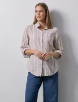 Camisa color beige con rayas verticales blancas, de lino, con cuello con solapa y abertura central con botones. Tiene un bolsillo aplicado en el pecho y mangas largas regulables con presilla y botón.