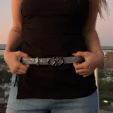 Cinturón plateado con brillos y hebilla metálica con diseño de doble círculo entrelazado.