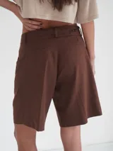 Bermuda negra de tiro medio, corte ancho, con bolsillos laterales y un ojal en la parte trasera.