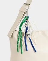Cartera tipo saca color crudo, de cuerina, con asa corta regulable para el hombro y cierre superior. Incluye charms decorativos colgantes.