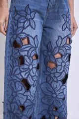 Pantalón de jean azul con bordados florales y aberturas en forma de flor en las piernas.