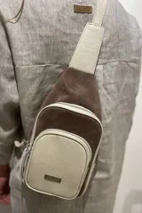 Mochila bandolera de cuero color marrón chocolate y detalles en color crema. Tiene dos bolsillos con cierre y correa regulable.