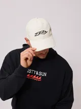 Gorra de gabardina color crudo con visera curva y logo de la marca bordado en negro en el frente.